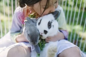 Une petite fille tient ses deux lapins dans ses bras.