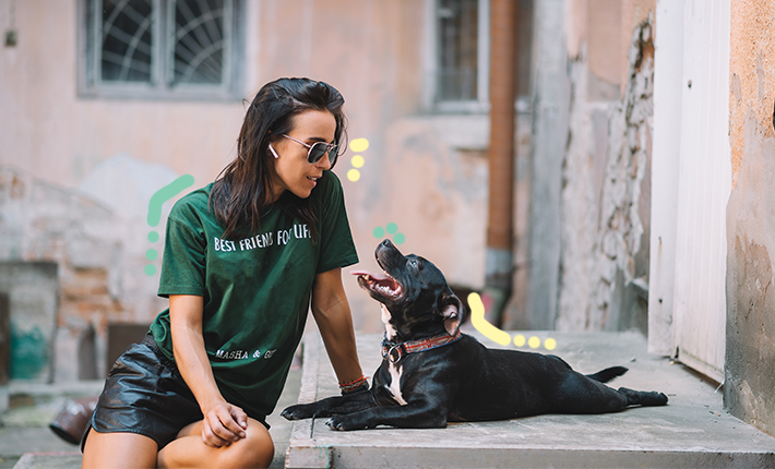 Une femme en chemise verte se détend sur une marche avec son chien noir assis à côté d'elle.